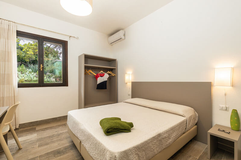 Bright bedroom with a double bed, bedside lamps, and a window overlooking greenery