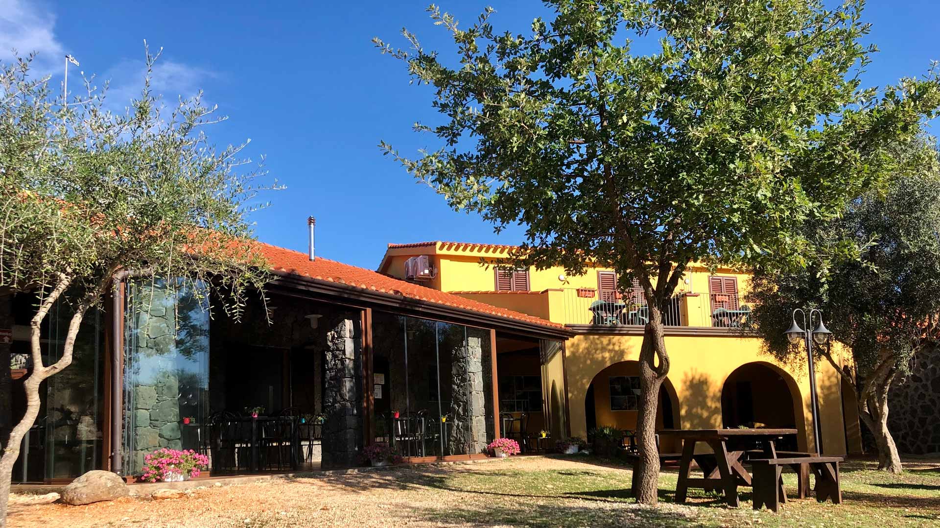 Sunny courtyard and arched veranda of a yellow villa with trees and outdoor seating