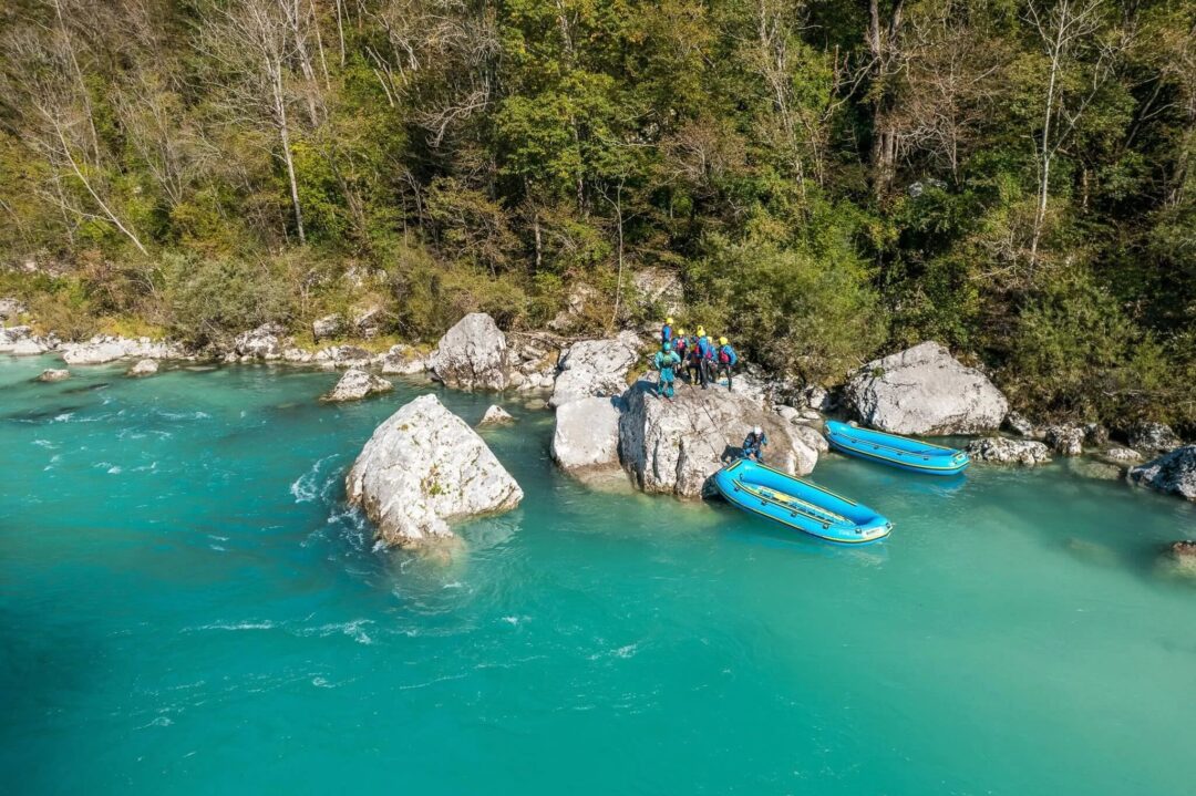 Kayaks on a turquoise river by rocky riverbank in a forested landscape