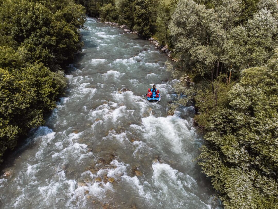 White-water rafting on a fast river through dense forest, with rafters in an inflatable boat
