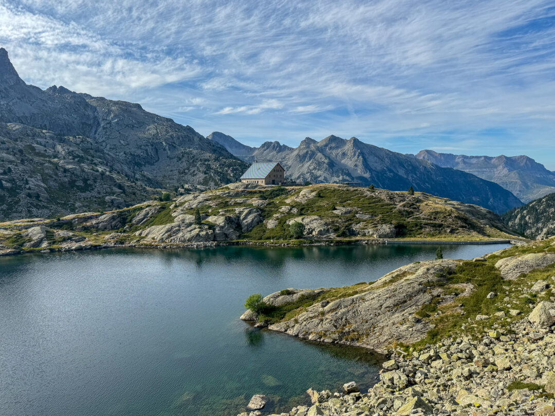 Mountain hut by a lake in the Spanish Pyrenees, with rugged peaks under a blue sky
