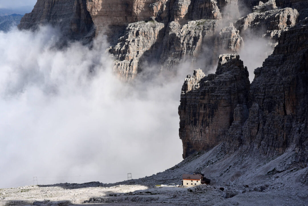 Dolomites rugged mountain cliffs with low cloud and a small mountain shelter hut at the base