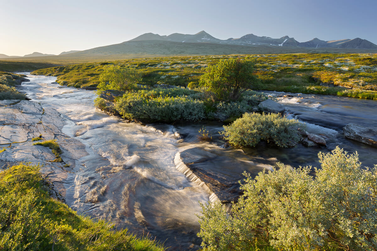 Scenic river winding through a green valley in Norway with mountains at sunrise