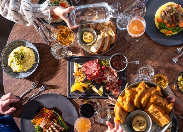 Friends toasting with drinks over a shared meal at a Norwegian restaurant table, with appetisers and bread.