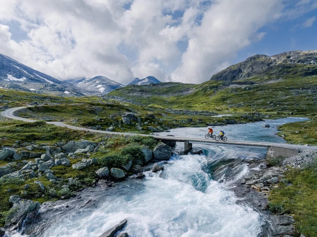 Cyclist rides over a bridge across river rapids in Norway’s mountain landscape