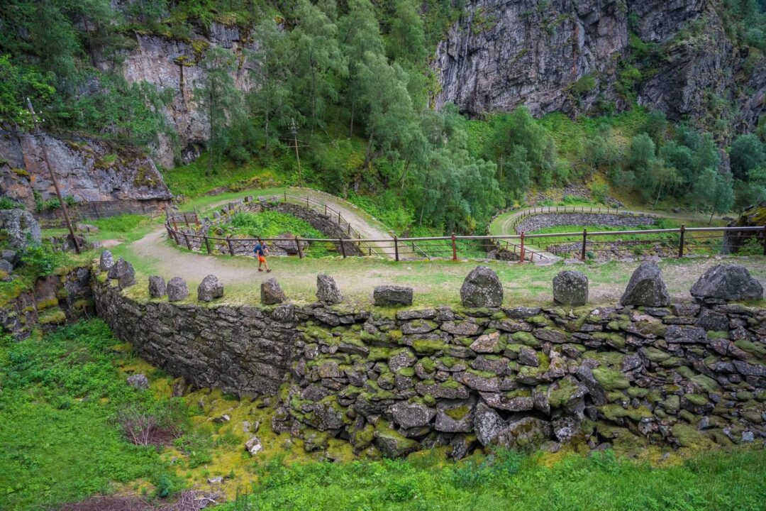 Hiking trail through a rocky valley in Norway, with stone walls and fenced paths by a stream