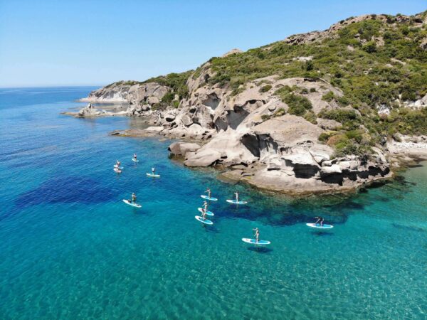 SUP paddleboards on calm turquoise water off a rocky Mediterranean coastline