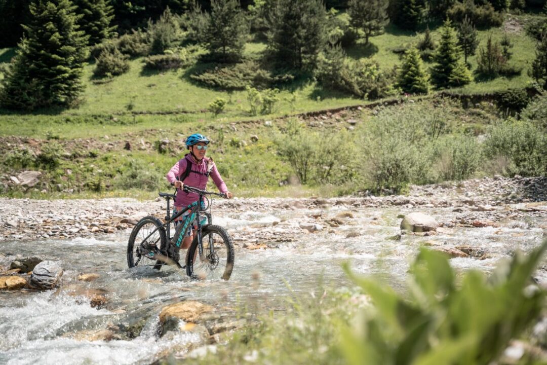 Woman mountain biking along a river through a green valley landscape with trees and hills