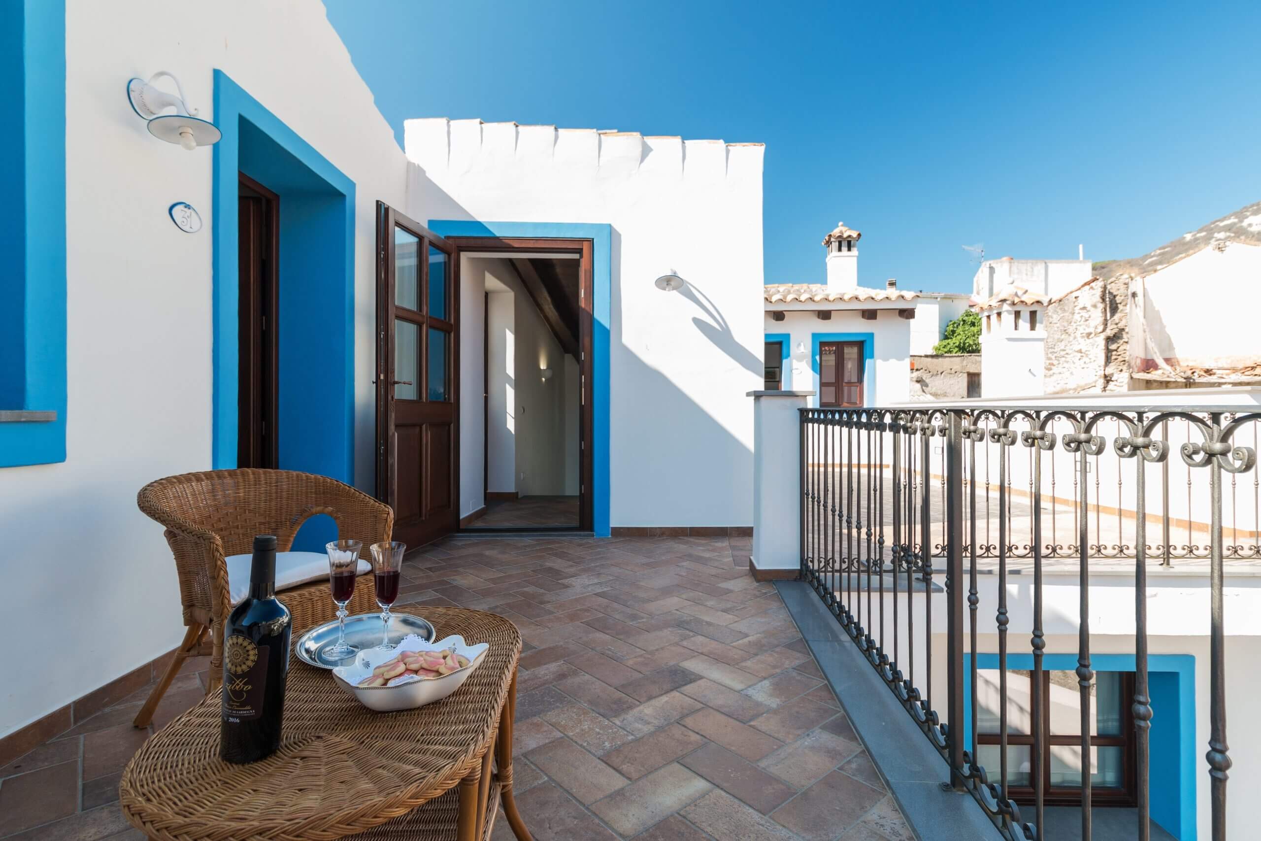 Blue-and-white Mediterranean terrace with wrought-iron railing, table with drinks, and mountain view