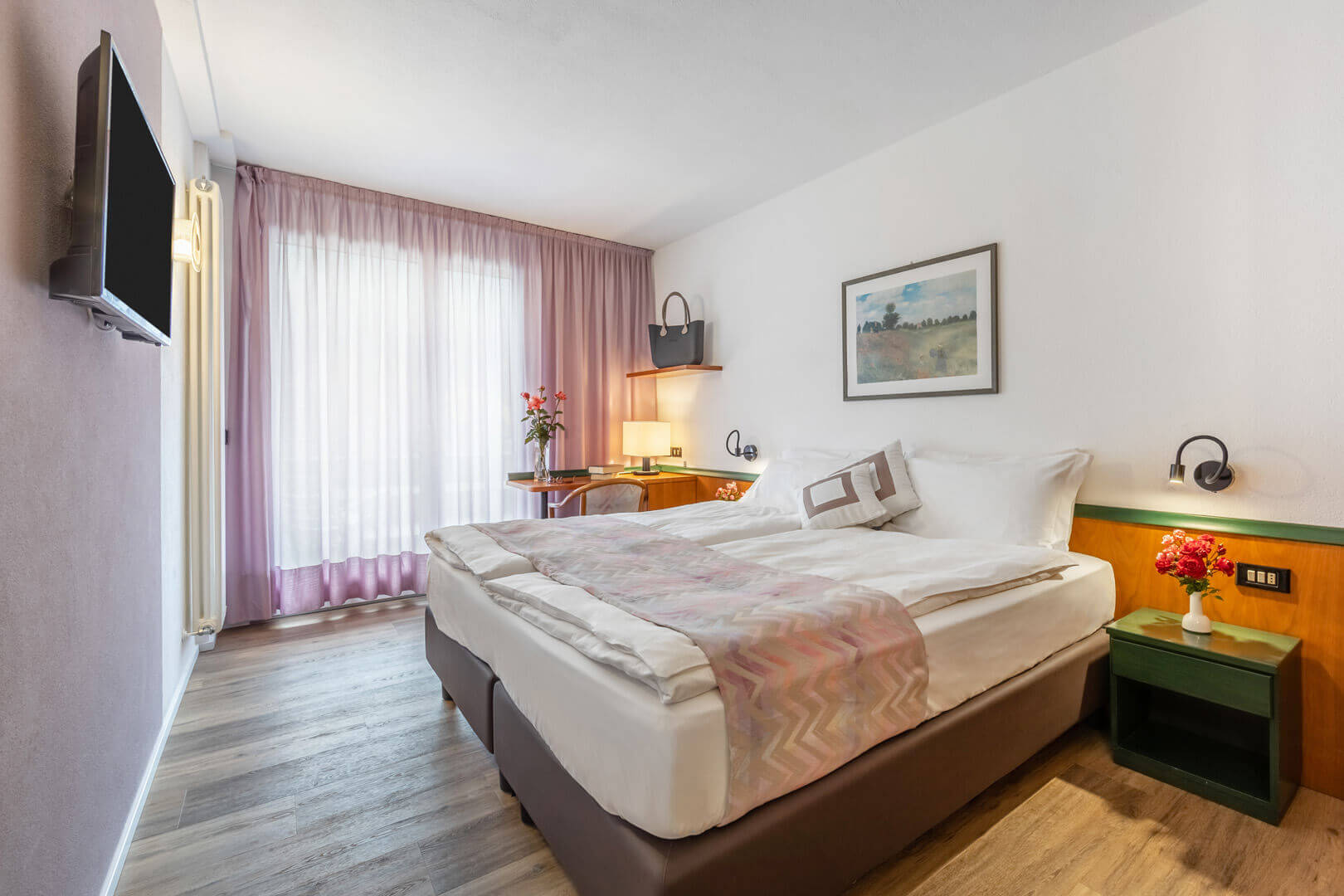 Bright hotel bedroom interior with double bed, curtains, bedside tables and green cabinet