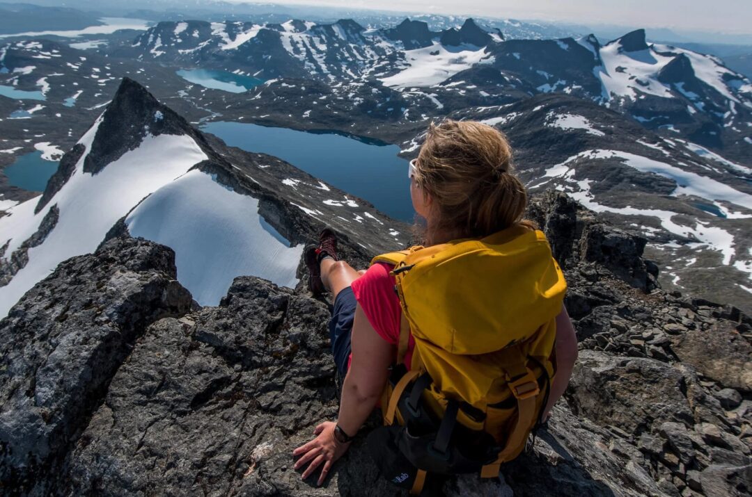 Woman hiking on a snowy mountain ridge above a lake in Jotunheimen, Norway