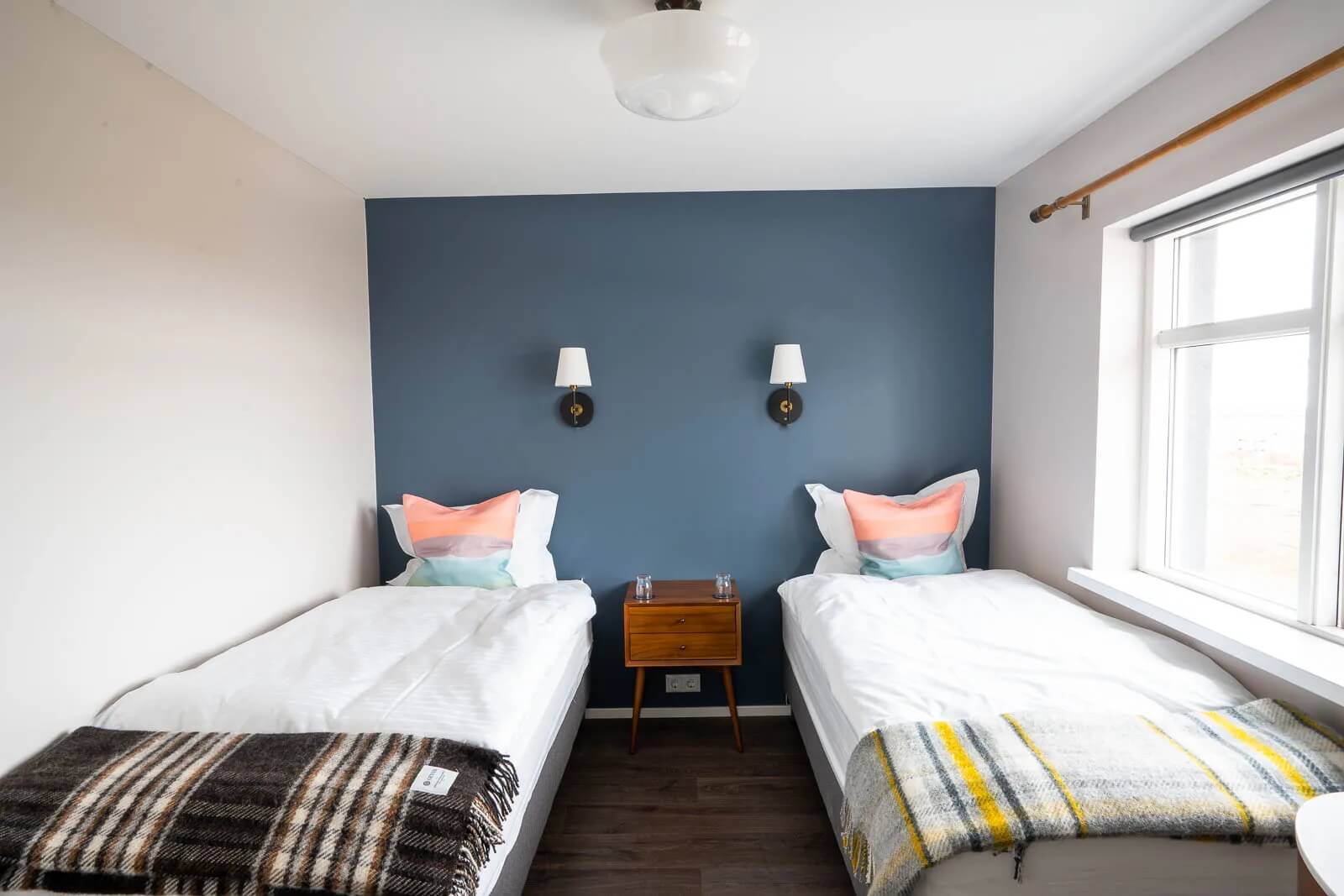Two beds in a bright bedroom with large windows and blue feature wall