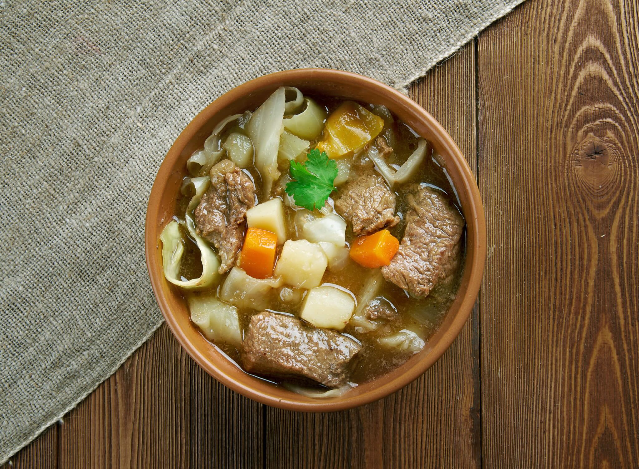Bowl of meat and vegetable stew with carrots, potatoes, onions and herbs