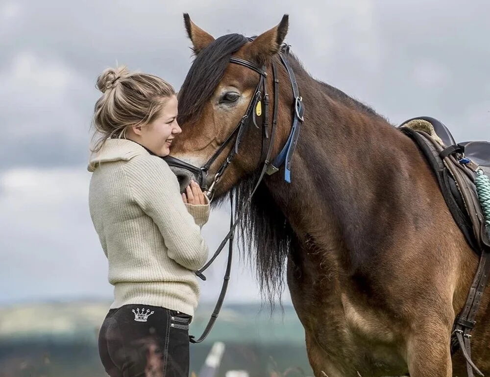 Woman cuddles a bridled horse during an outdoor riding session by the sea