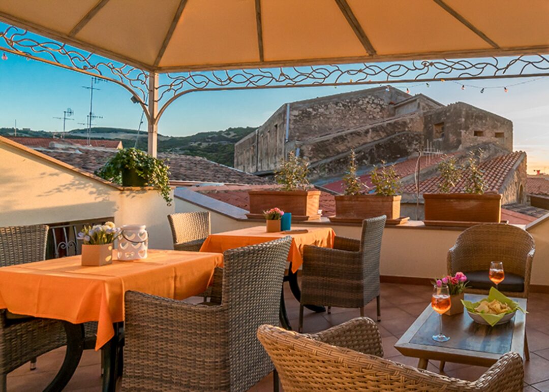 Outdoor terrace dining set under a canopy with orange tablecloths and a countryside view at sunset