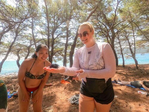 Two women stand on a sandy beach by the sea with boats and gear nearby in Croatia