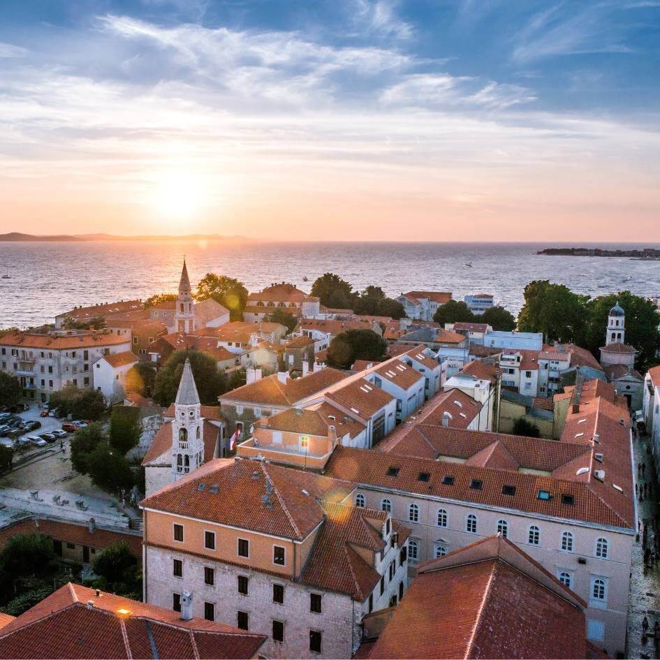 Aerial view of a Croatian coastal town at sunset with red-roofed buildings and sea