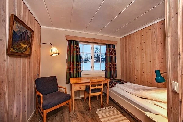 Norwegian wooden cabin bedroom with single bed, chair, desk and window view.
