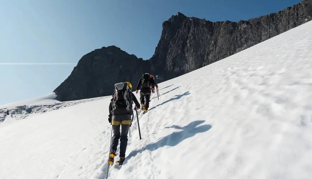 Women hiking on snow-covered mountains with trekking poles against steep rocky peaks