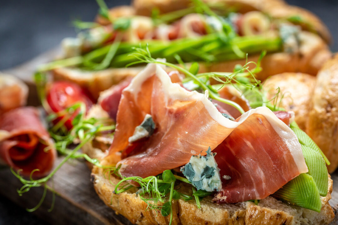 Prosciutto and rocket bruschetta topped with salad greens and sprouts on rustic bread