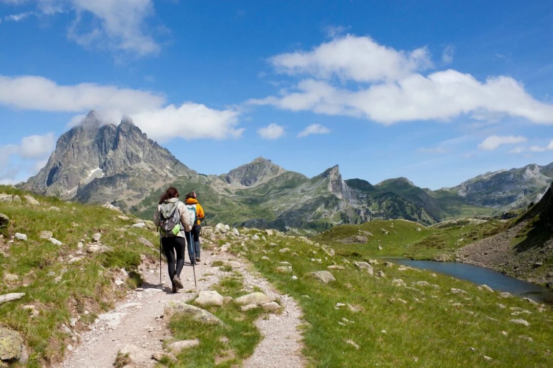 Women hike along a mountain path in the Spanish Pyrenees with a lake and rugged peaks in view