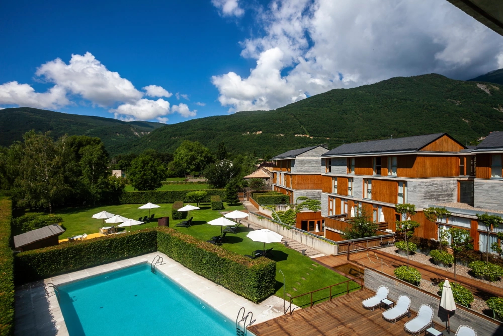 Lodge buildings with outdoor swimming pool, set in a green mountain valley beneath blue skies