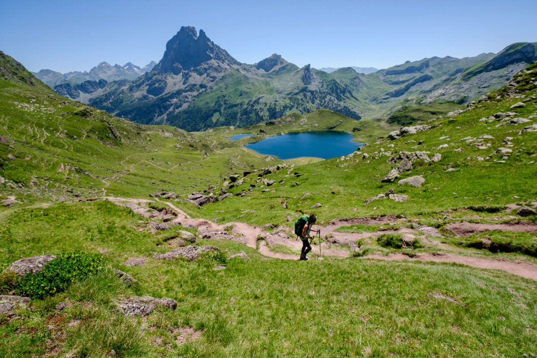 Women hiking a mountain trail in the Spanish Pyrenees above a blue lake and alpine peaks