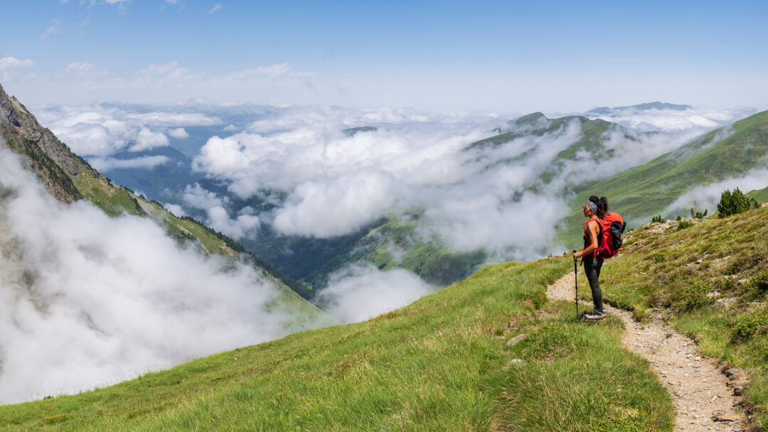 Women hiking a trail on a grassy ridge above clouds in the Spanish Pyrenees
