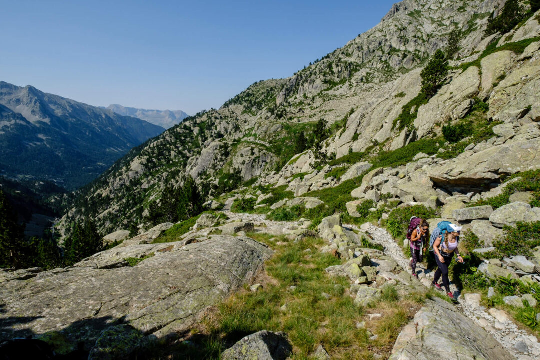 Hikers trekking along a rocky mountain trail with a vast valley view in the Pyrenees