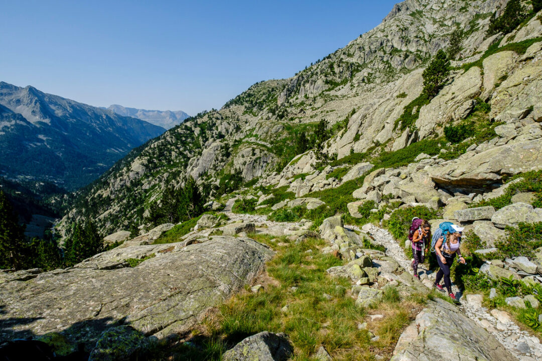 Women hiking a rocky mountain trail in the Spanish Pyrenees under a clear blue sky