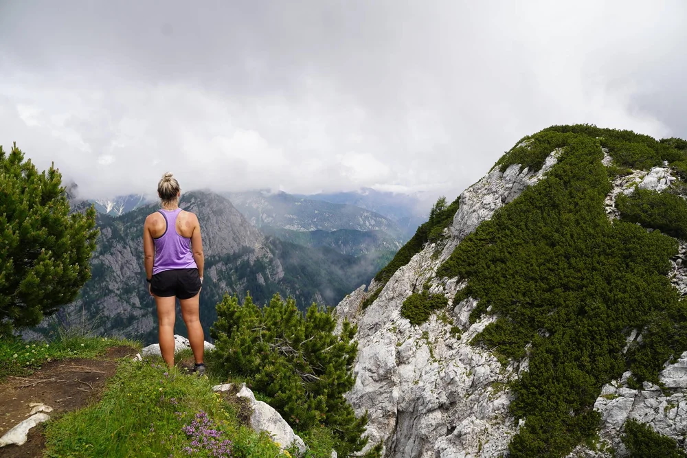 Woman hiking along a rocky ridge with mountains and clouds, Slovenia