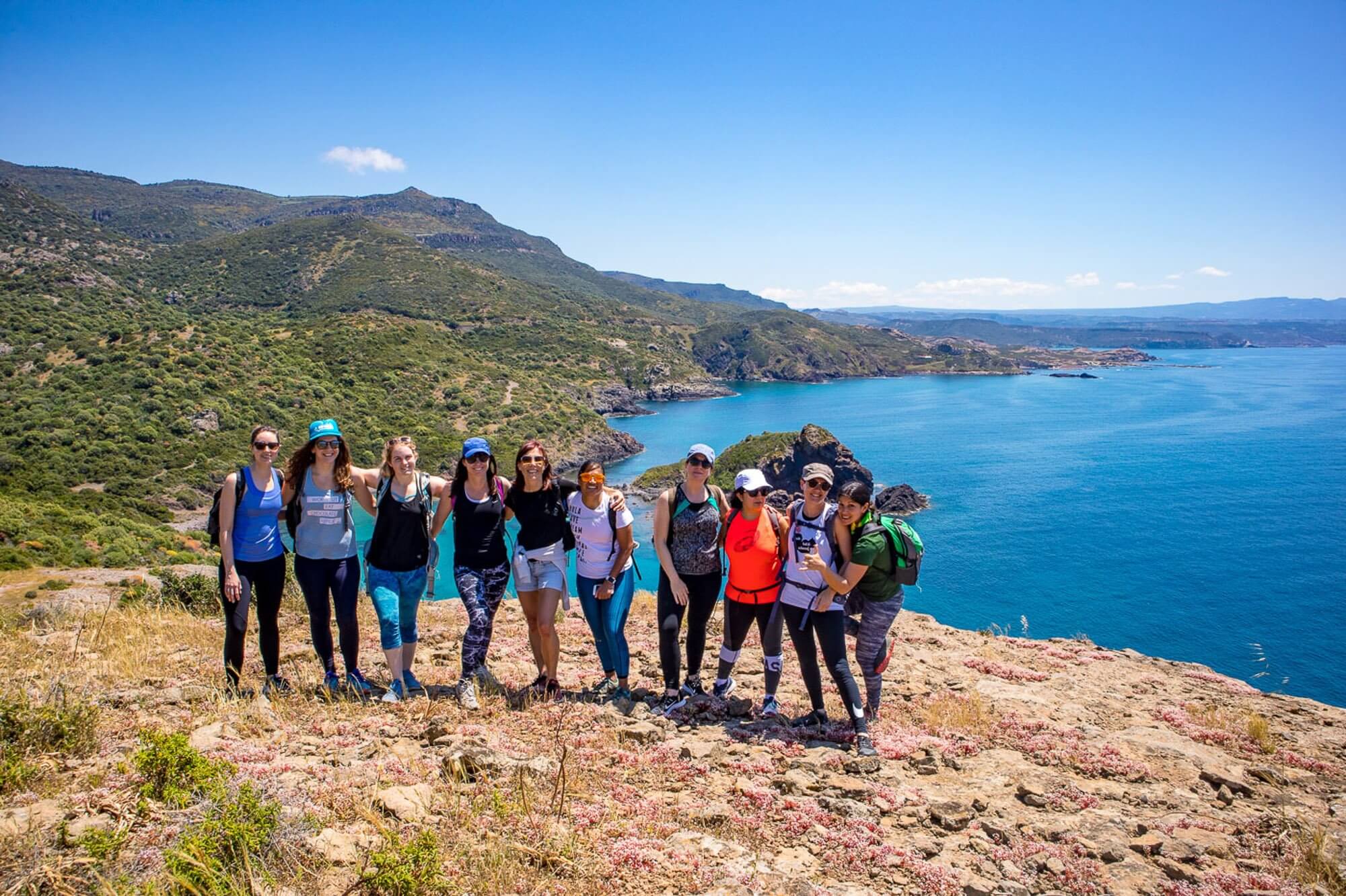 Women hiking on a coastal viewpoint, overlooking blue sea and surrounding hills on the Mediterranean coast