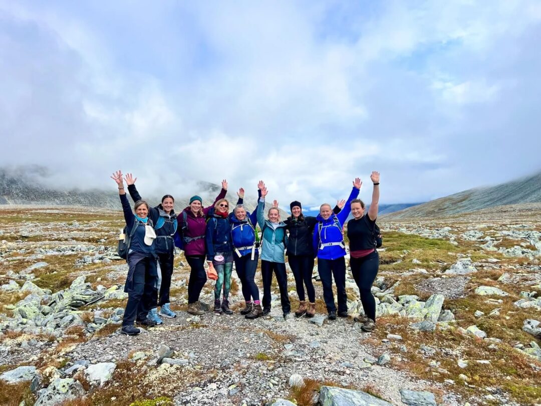 Women hiking on a rocky Norwegian landscape, arms raised on a misty day