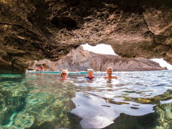 Women paddle on SUP boards in a sea cave with clear water and rocky cliffs