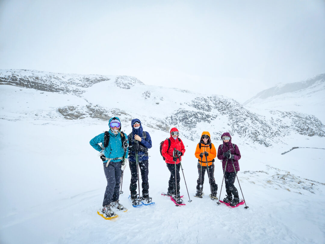 Women snowshoe hikers standing in snowy mountains under a clear winter sky