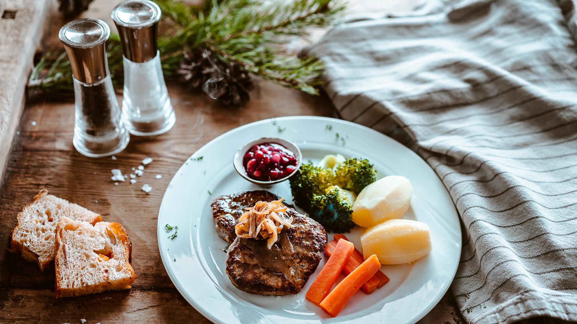 Plate of food with roasted meat, vegetables and berry dessert on a table with candles and bread