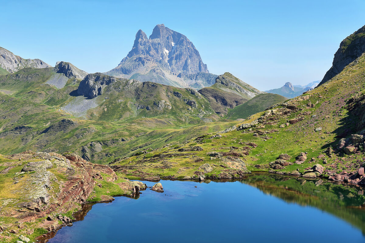 Spanish Pyrenees alpine valley landscape with a blue mountain lake and rugged peaks in clear sky