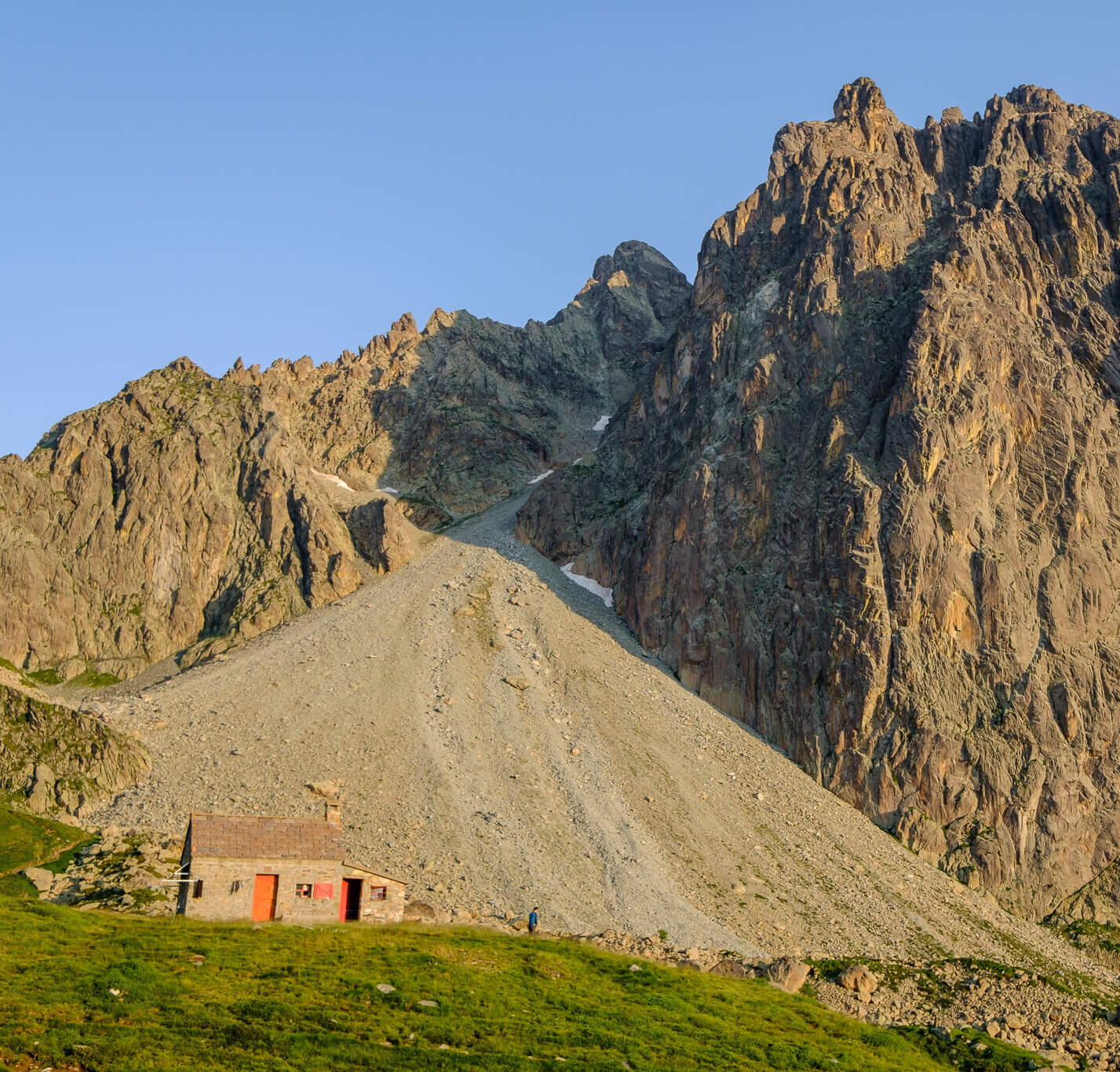 Mountain hut and hiking trail by rocky peaks in the Pyrenees at golden hour