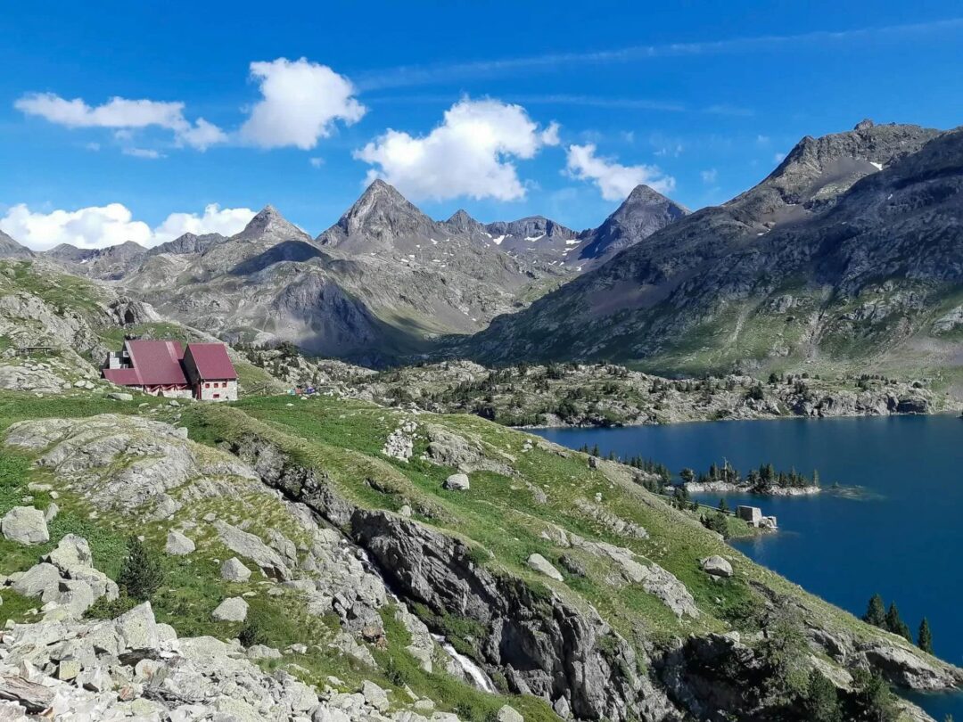 Mountain hut and lake view along a hut-to-hut trek in the Pyrenees, with rugged peaks under blue sky