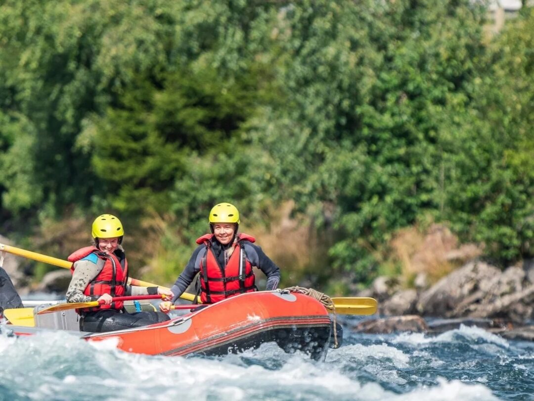 Women in helmets white-water rafting on an orange inflatable raft in rapids