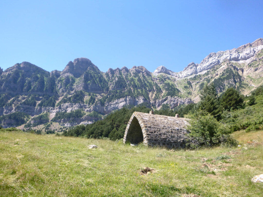 Hiking landscape in the Spanish Pyrenees with a stone shelter in a grassy mountain valley