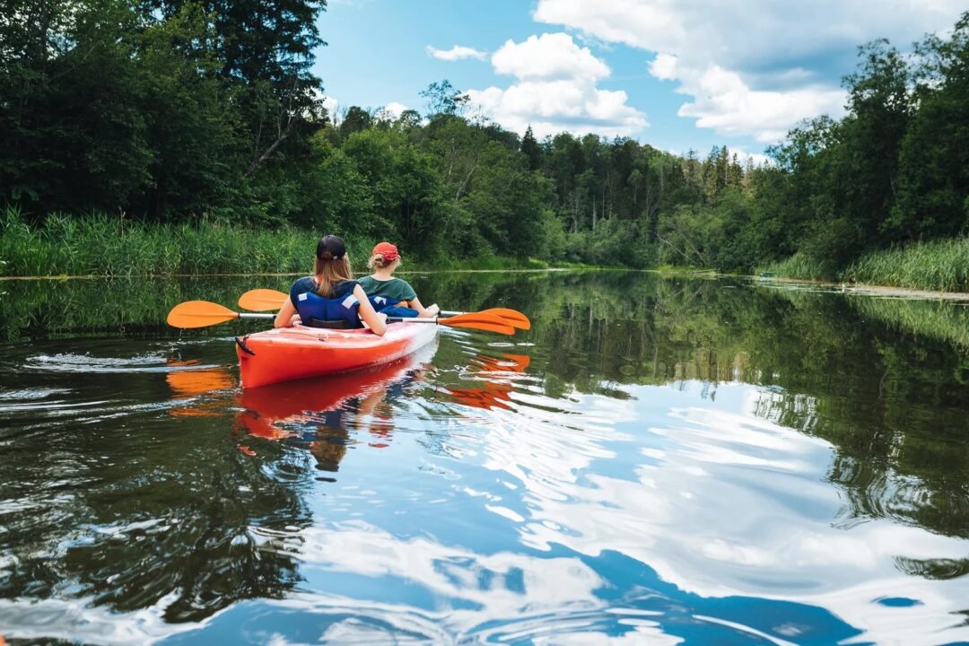 Women kayaking on a calm lake surrounded by forest, outdoors adventure activity