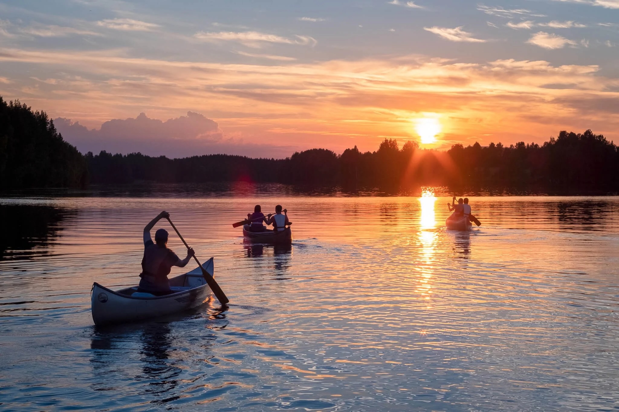 Women kayaking on a calm lake at sunset, part of a wilderness adventure holiday