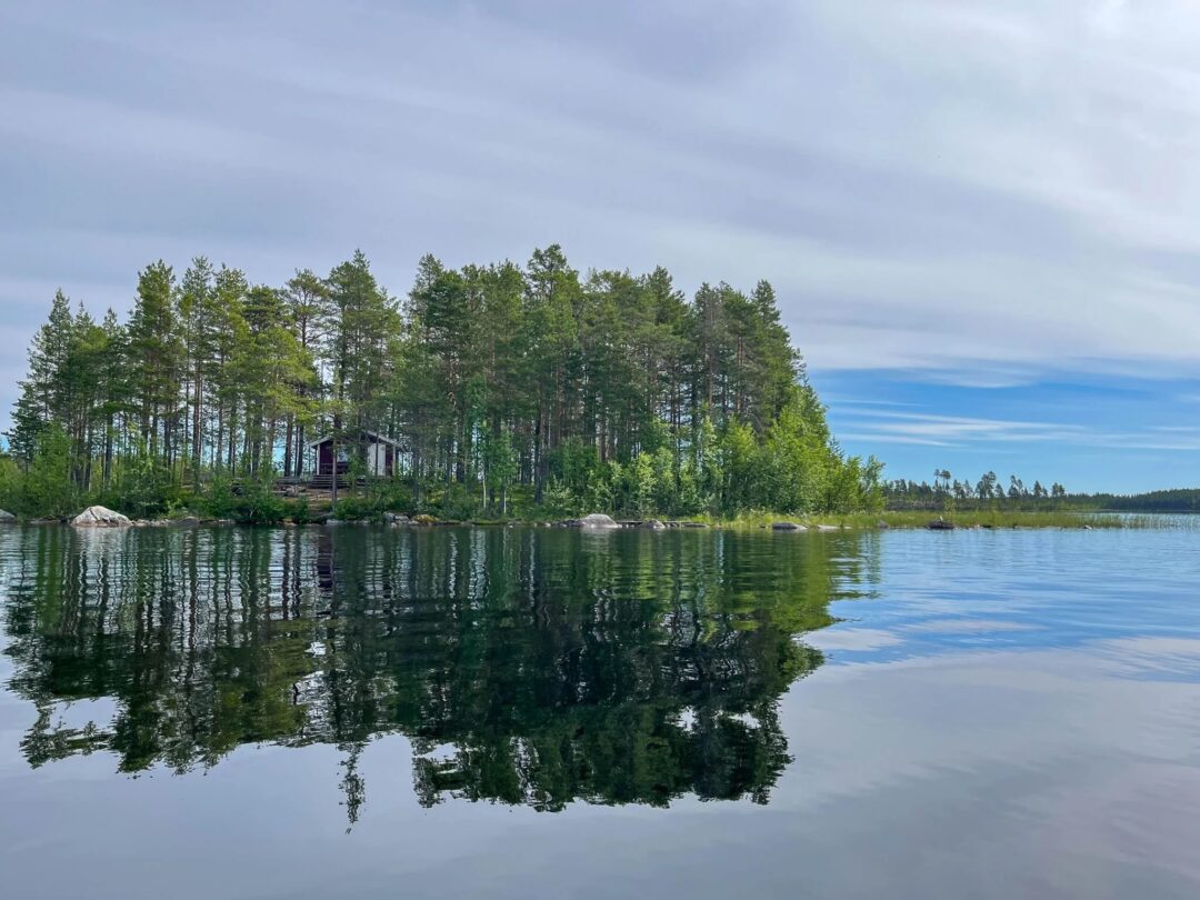 Calm lake with pine forest reflection and a small lakeside cabin among trees