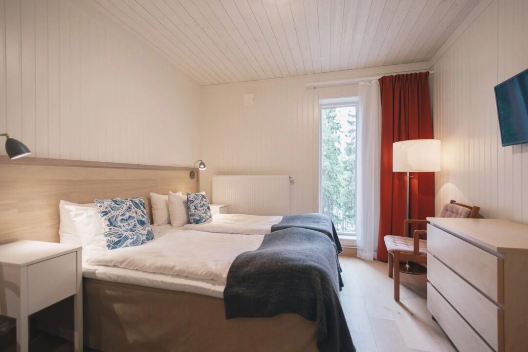 Bright bedroom interior with an unmade double bed, curtains, and bedside lamps