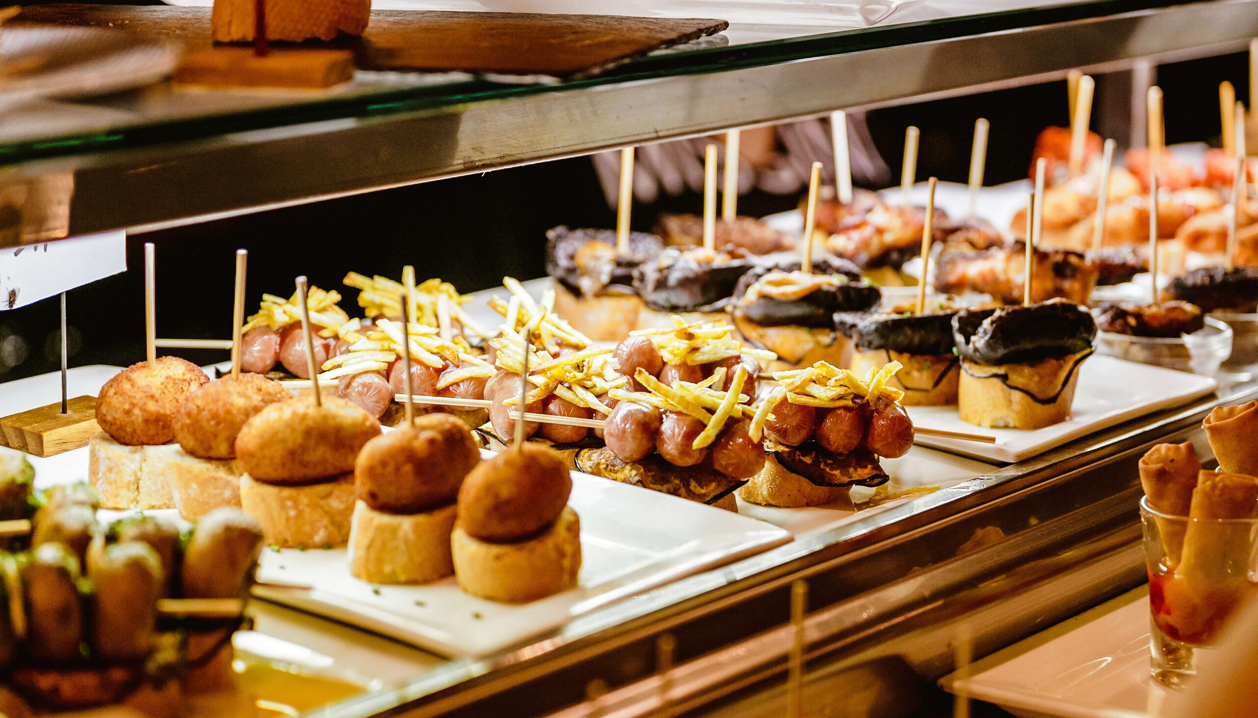 Tray of appetisers and small bites at a buffet table, including pastries and skewers under warm lights