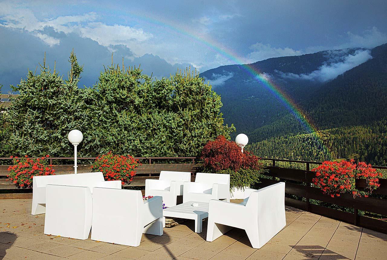 Outdoor terrace with white seating, flowers and rainbow over the Italian Dolomites mountains in Italy