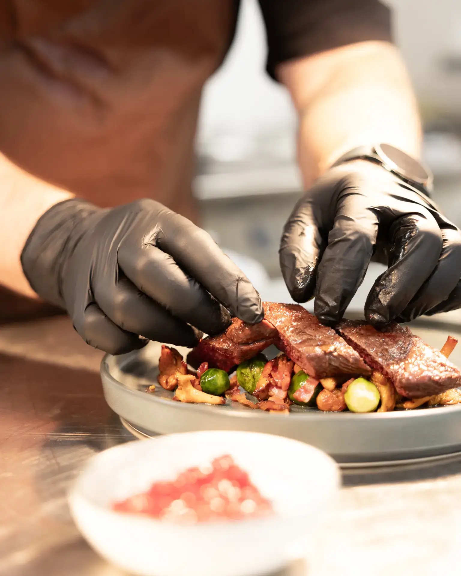 Gloved hands preparing a meal, chopping and plating ingredients in a bowl