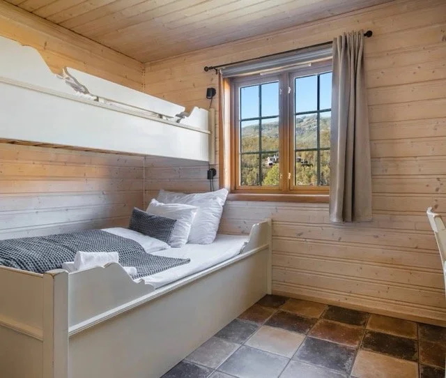 Cozy wooden cabin bedroom with unmade bed and large window overlooking mountain landscape in Norway