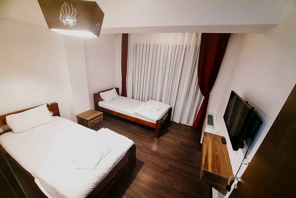 Twin beds in a hotel room with curtains, bedside tables and a wall-mounted TV